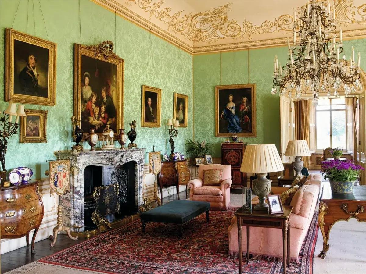 A drawing room at Highclere Castle with green silk walls, gilded family portraits and a crystal chandelier