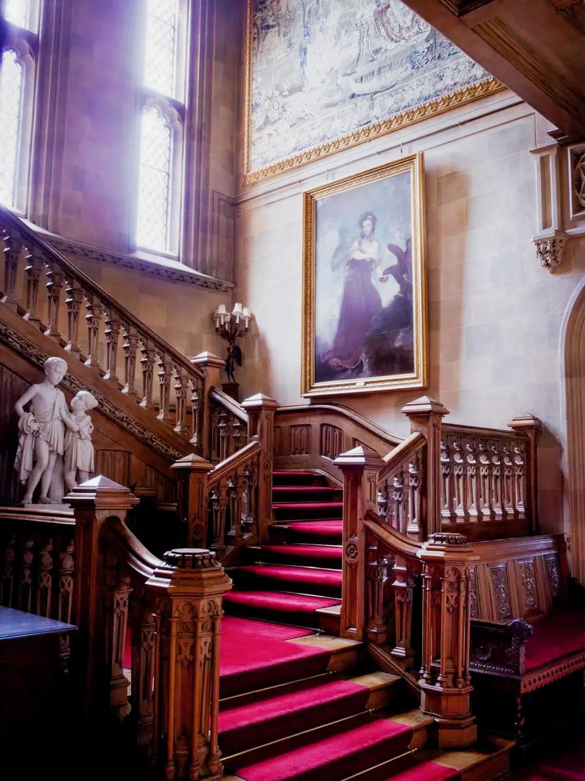 The carved oak grand staircase at Highclere Castle with a red carpet runner