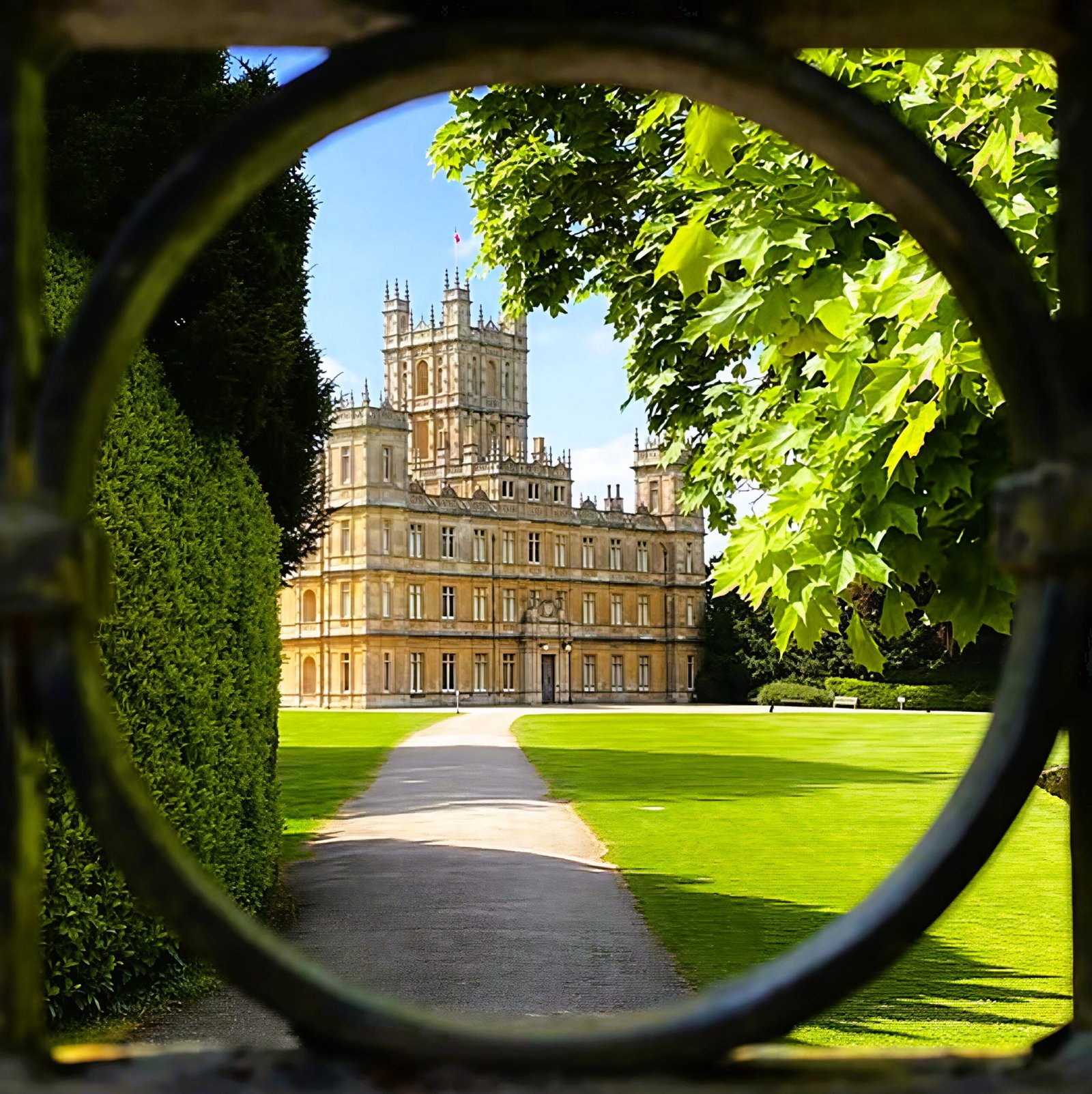 Highclere Castle framed by trees and a circular garden gate at the end of a path